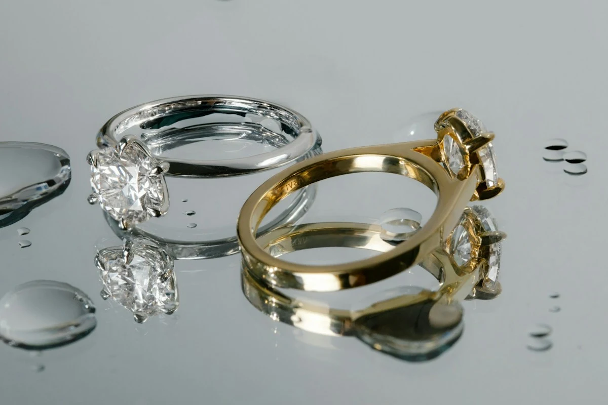 Two diamond solitaire rings reflected on a surface with water droplets